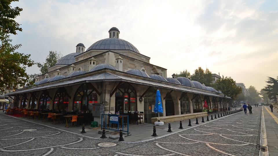 A historic building with a large dome and arched windows, surrounded by cobblestone pavement and outdoor seating.