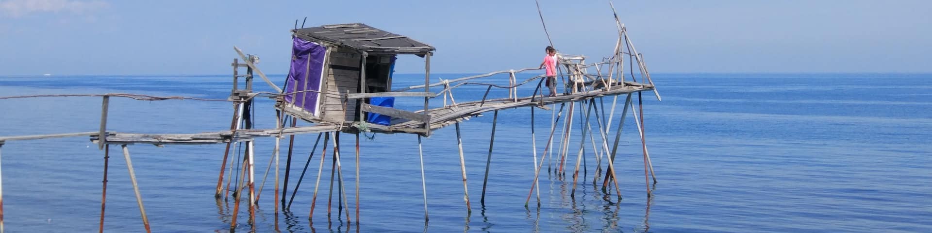 A wooden pier extending into calm waters, with a small shelter and a person standing on it.