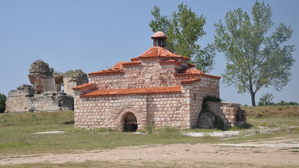 A historic stone building with a red-tiled roof and arched entrance.