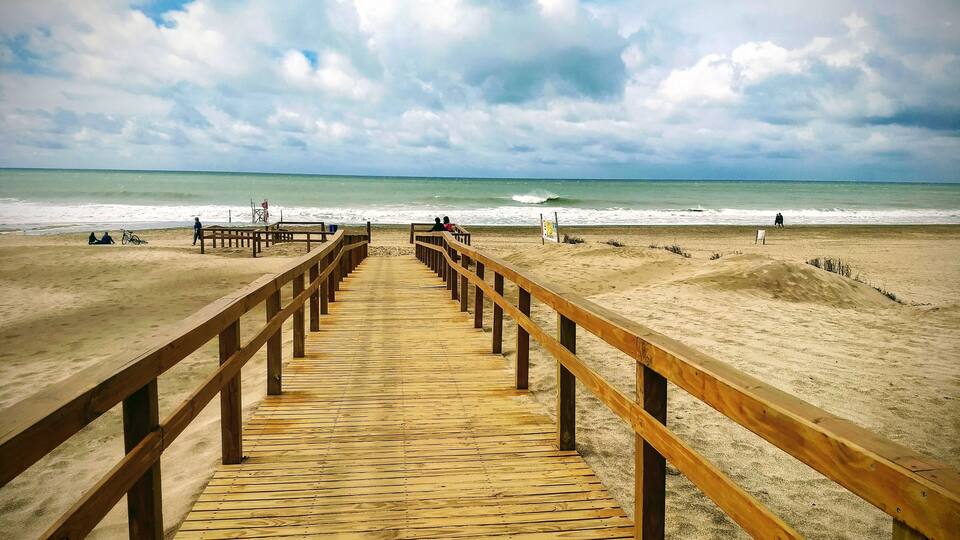 A wooden boardwalk leading to a beach with waves in the background.