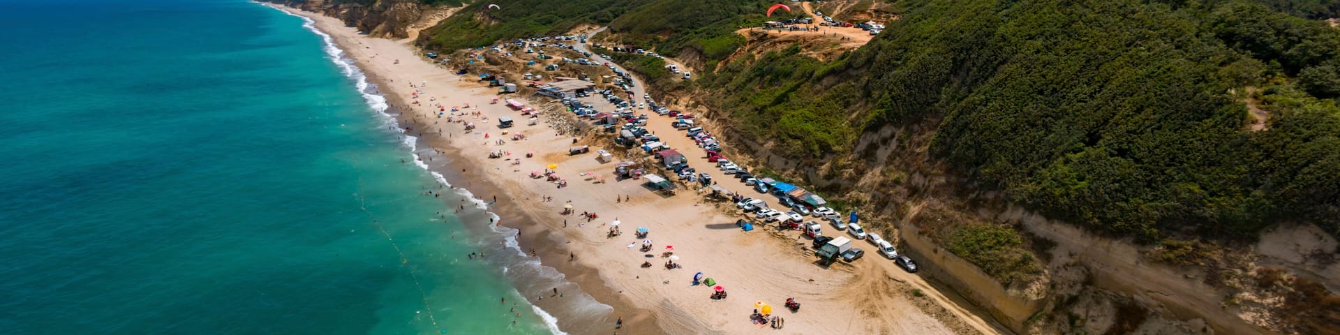 Aerial view of Ormanli beach with paragliders and umbrellas along the tranquil Black Sea coastline, Catalca, Turkey.