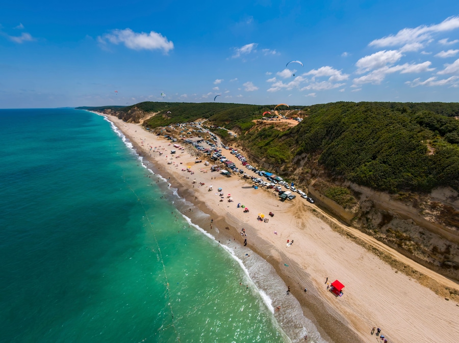 Aerial view of Ormanli beach with paragliders and umbrellas along the tranquil Black Sea coastline, Catalca, Turkey.
