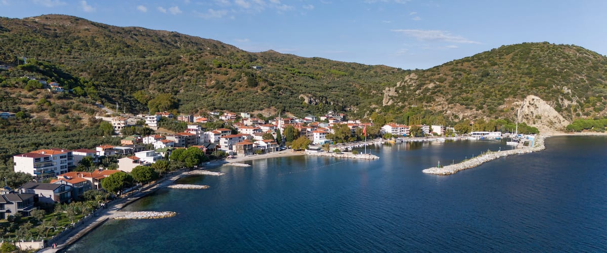 A coastal town with buildings along the waterfront, a clear blue sea, and hills in the background.