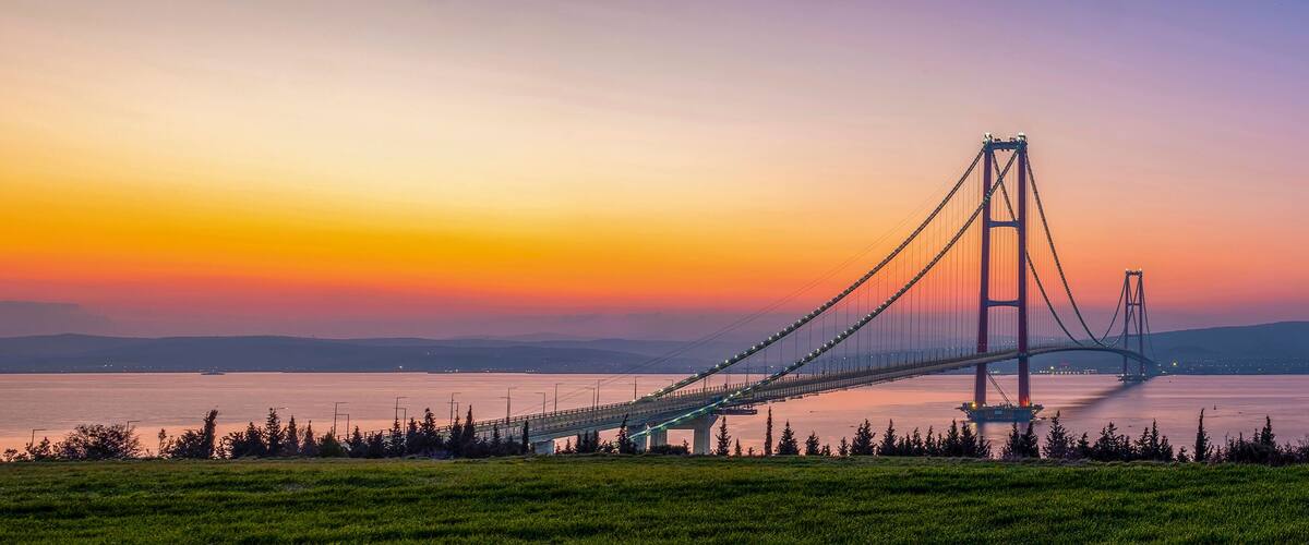 A suspension bridge at sunset with a clear sky and calm water.