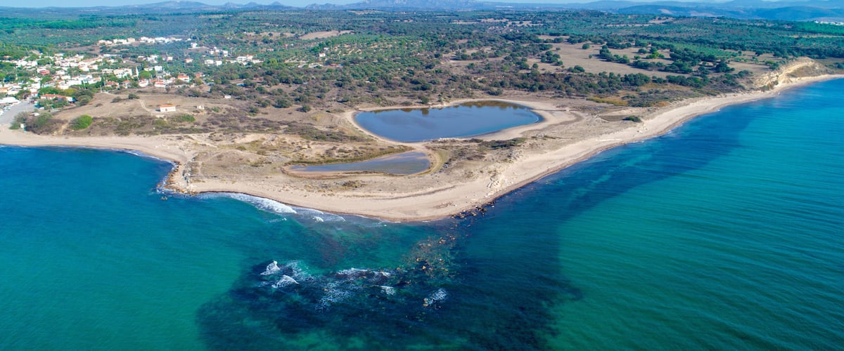 An aerial view of a coastal area with a beach, a small lake, and a town in the background.