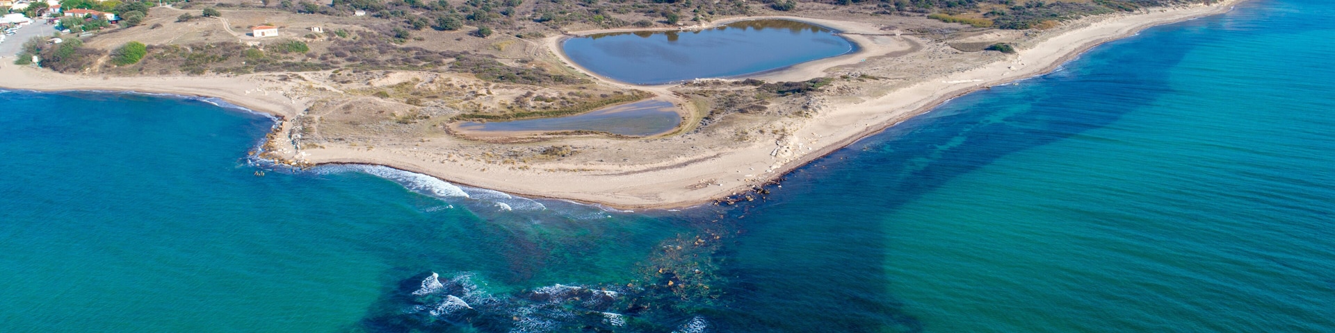 An aerial view of a coastal area with a beach, a small lake, and a town in the background.