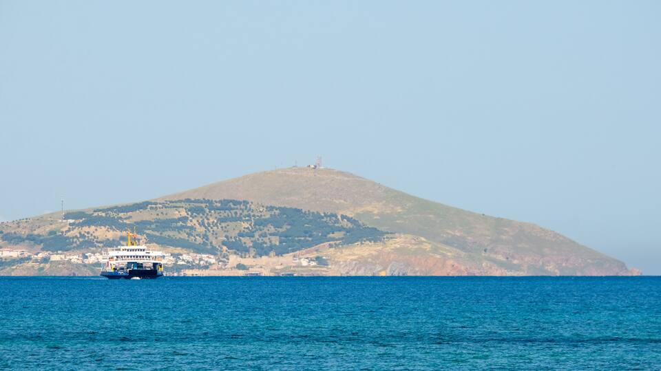 A ferry in the sea with a hill in the background.