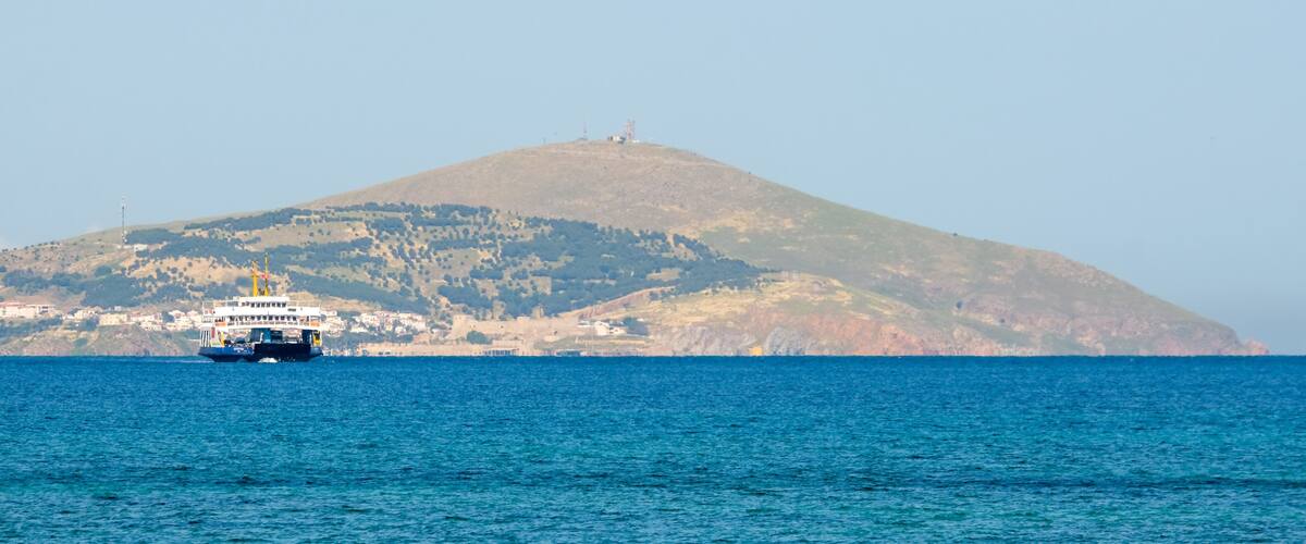 A ferry in the sea with a hill in the background.