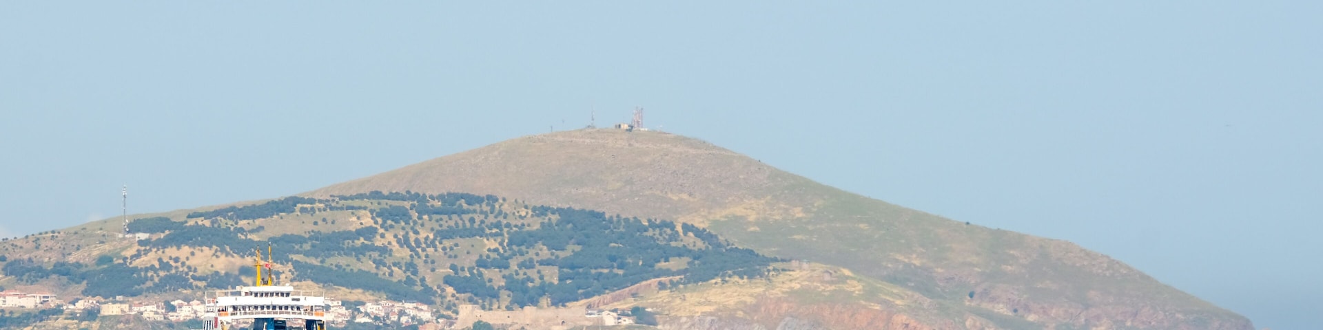 A ferry in the sea with a hill in the background.