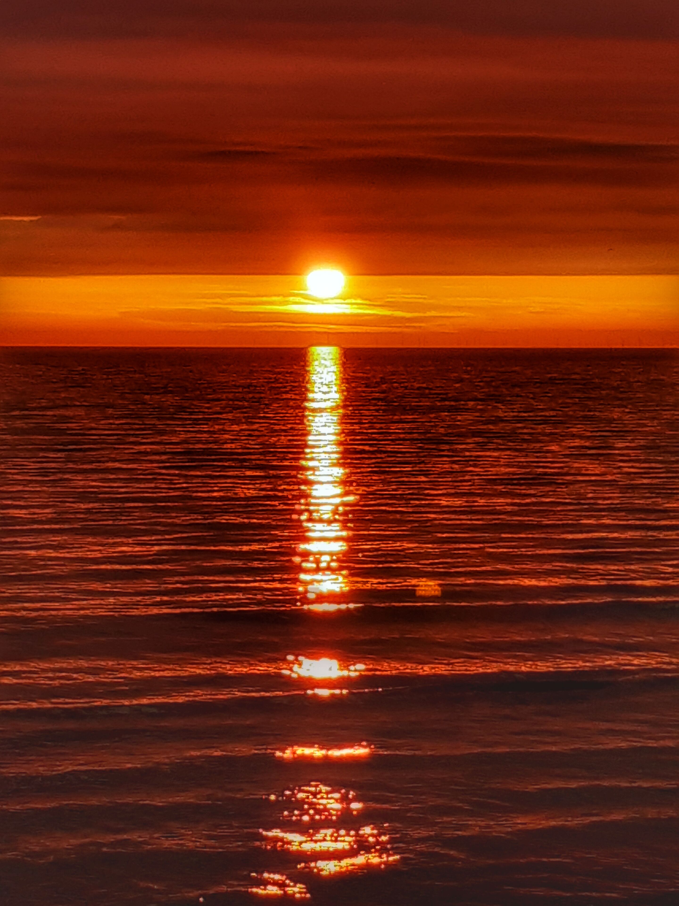 A sunset over the ocean with a visible sun reflection on the water.