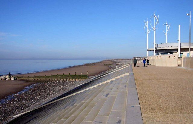 A coastal promenade with a pebble beach, a stone pathway, and a building with a flat roof.