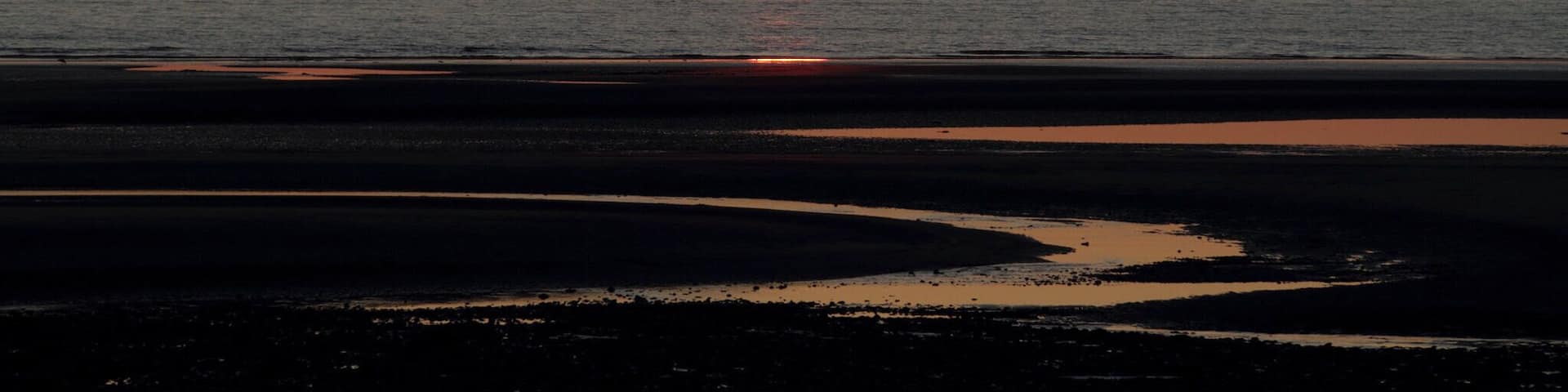 A sunset over a calm sea with a visible horizon line and a beach in the foreground.