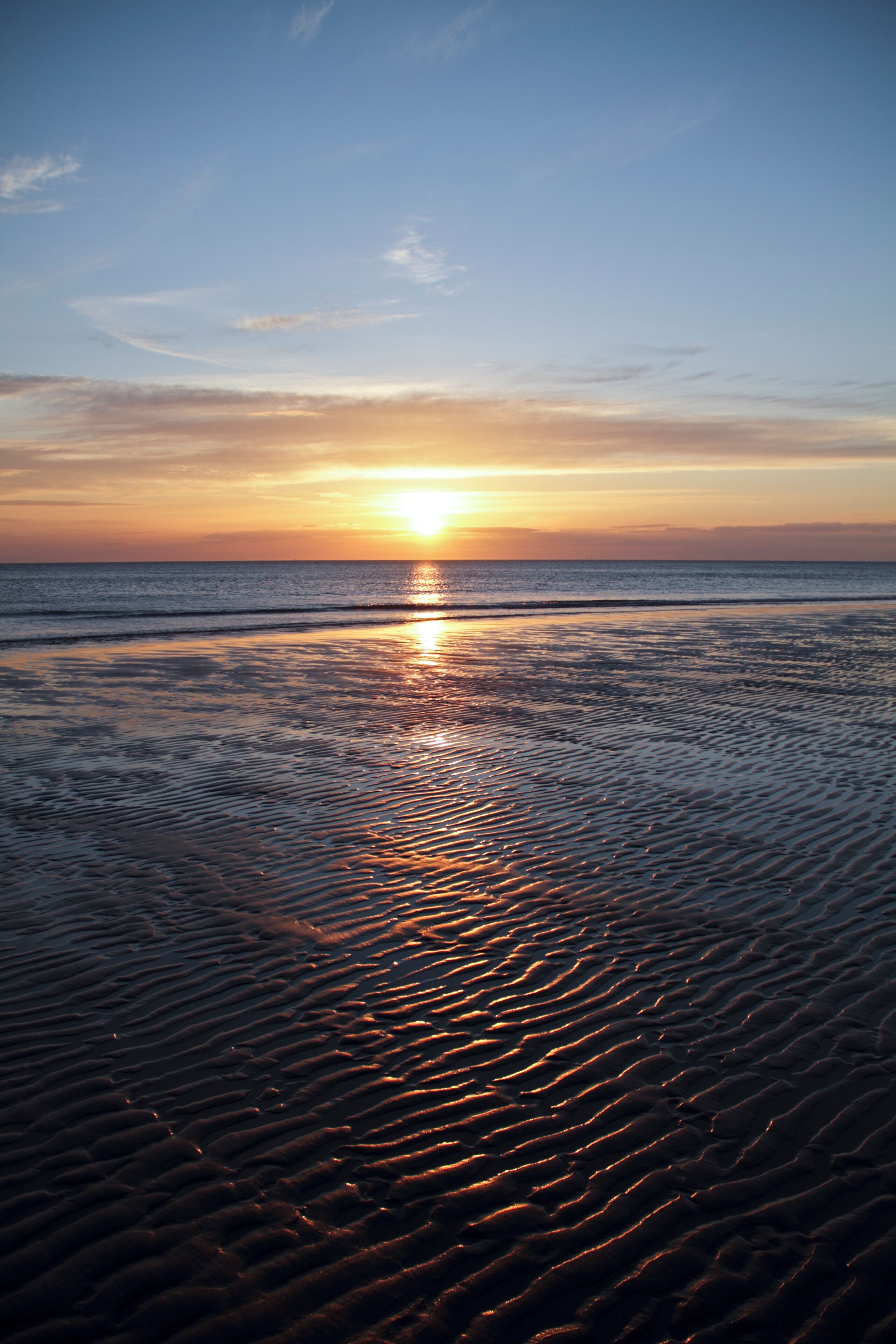 A sunset over a beach with waves reflecting the sun's light.