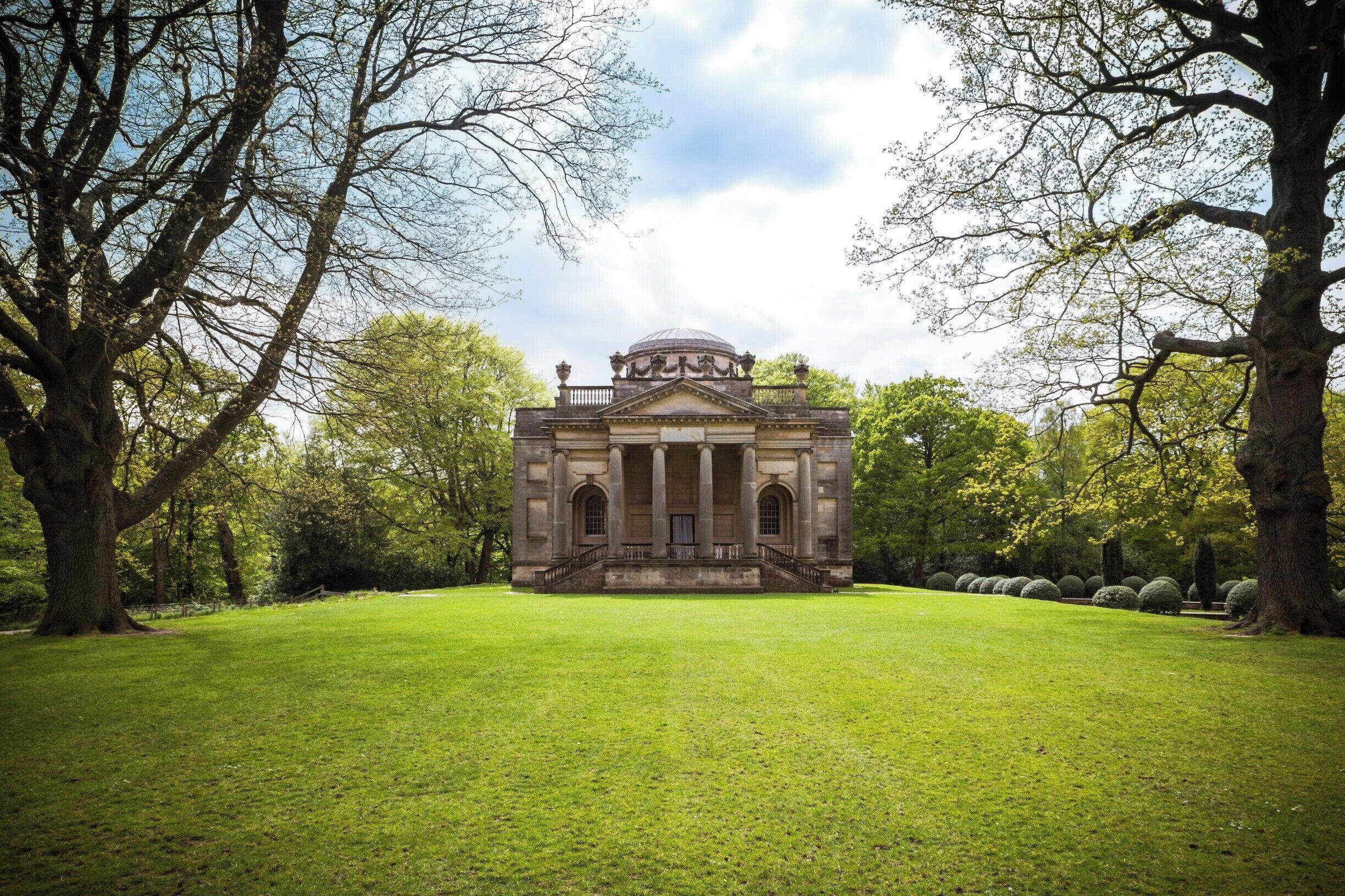 A classical building with a dome and columns, surrounded by a well-manicured lawn and trees.