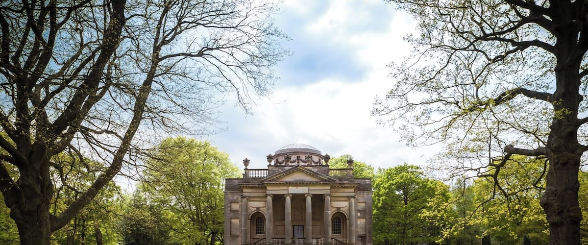 A classical building with a dome and columns, surrounded by a well-manicured lawn and trees.