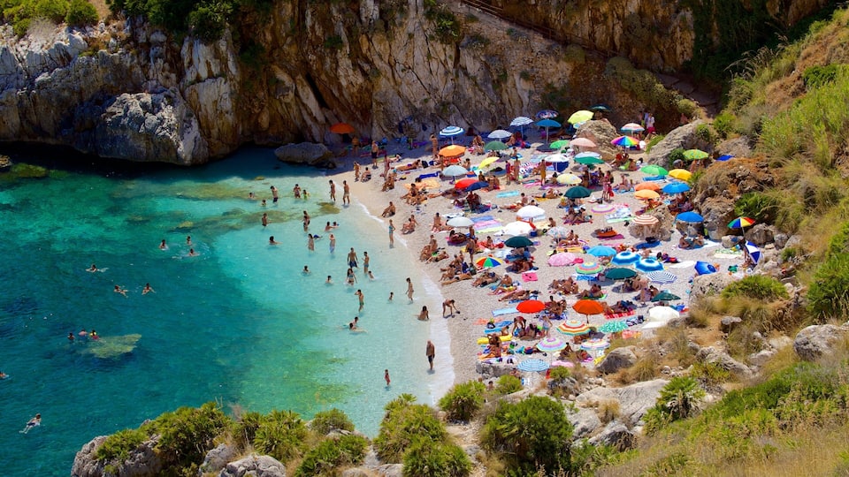 A crowded beach with clear turquoise water and rocky cliffs.