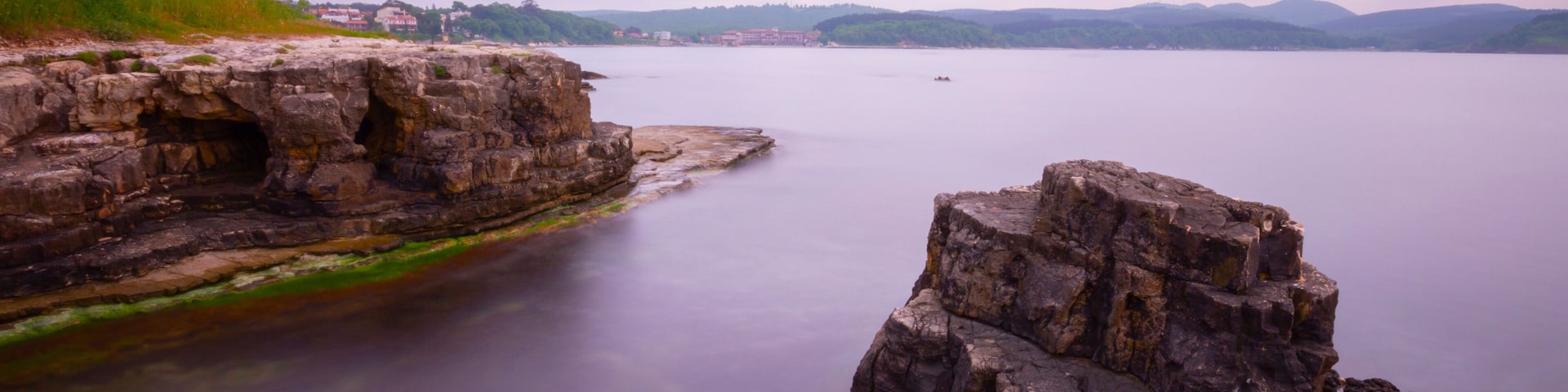 Un lago tranquilo con formaciones rocosas y edificios a lo lejos.
