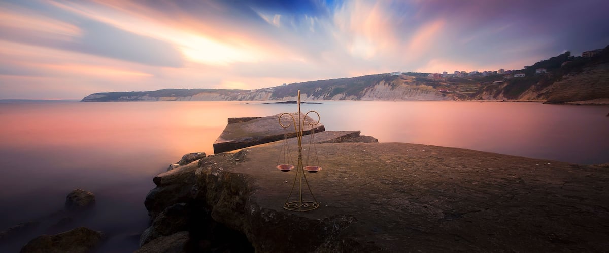 A coastal landscape with a calm sea, rocky cliffs, and a sunset.