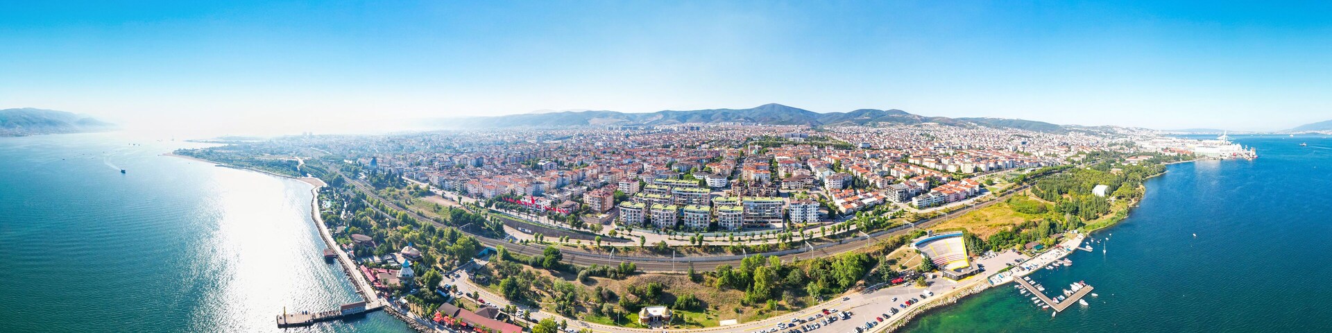An aerial view of a coastal city with a central roundabout, a marina, and a large body of water.