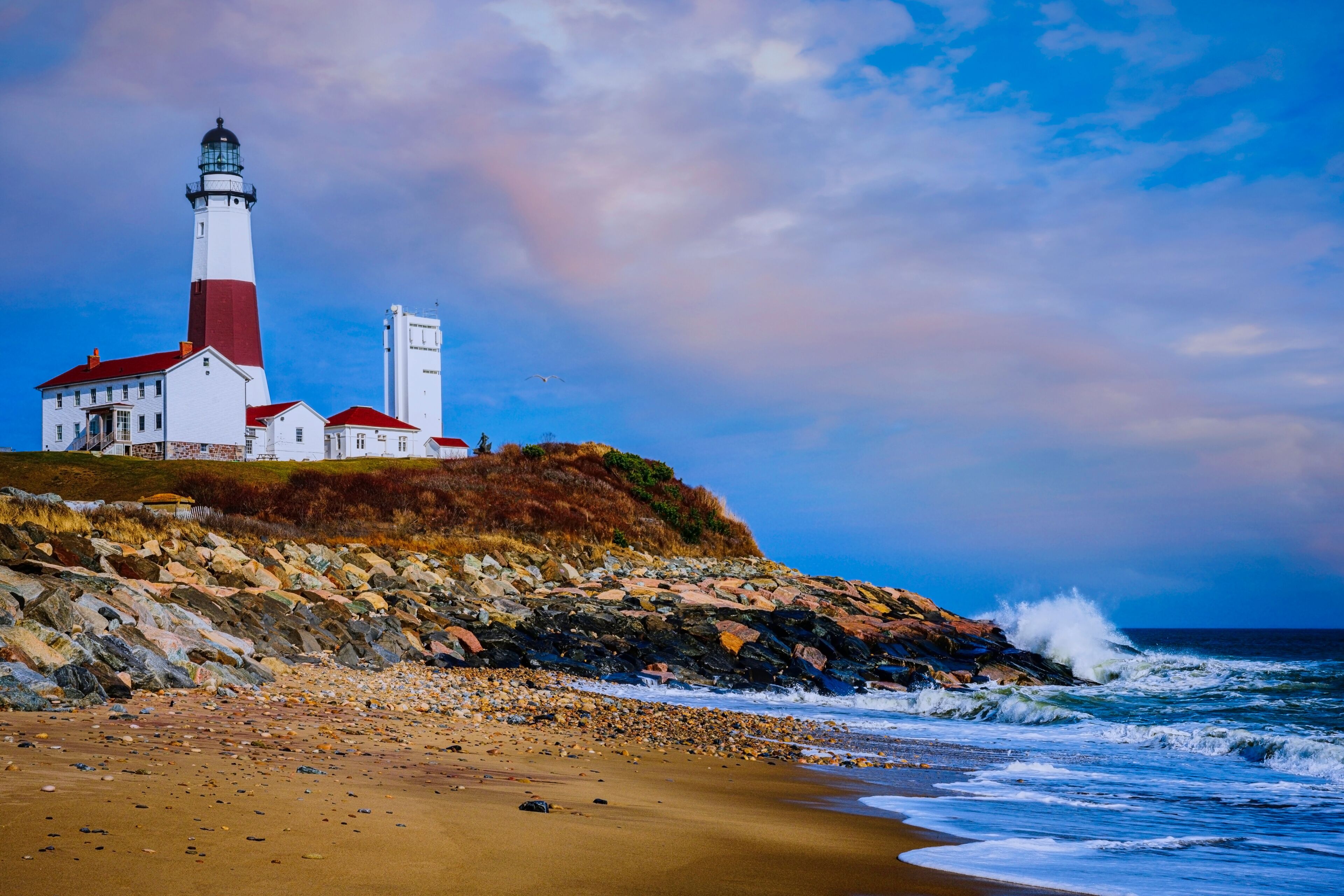 A lighthouse on a rocky cliff by the sea, with waves crashing against the shore.
