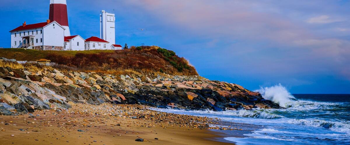 A lighthouse on a rocky cliff by the sea, with waves crashing against the shore.