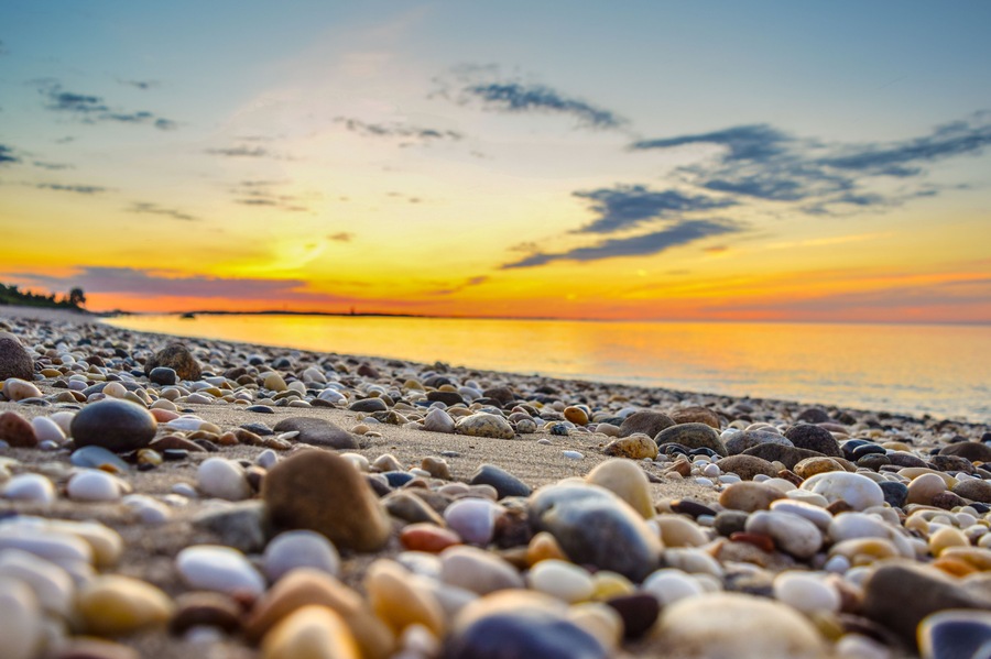 Una playa de guijarros al atardecer con un mar tranquilo y un cielo despejado.
