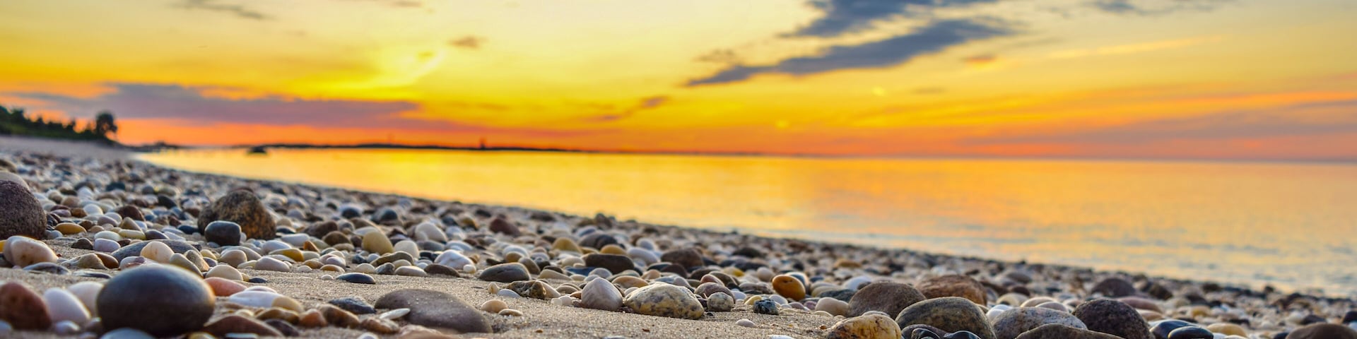 Una playa de guijarros al atardecer con un mar tranquilo y un cielo despejado.