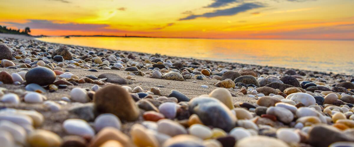 A pebbled beach at sunset with a calm sea and a clear sky.