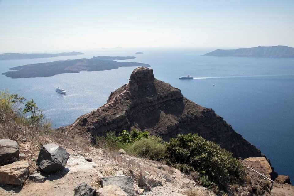 Un penya-segada rocosa amb vista a un mar tranquil, un vaixell de creuer i un veler.