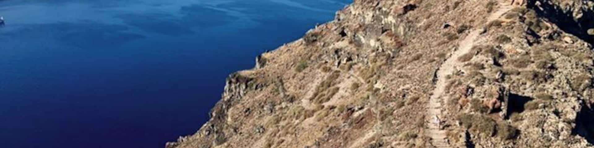 Um litoral acidentado com uma formação rochosa imponente e uma trilha descendo até o mar.