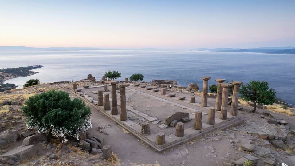 Ancient ruins with columns and a view of the sea.