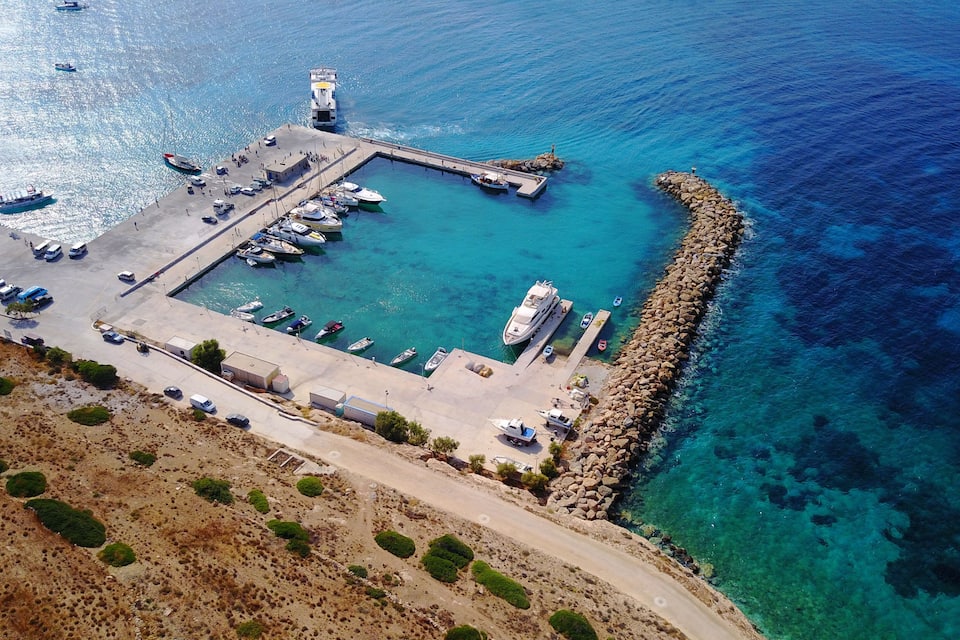 Vista aérea de uma marina costeira com barcos atracados, um farol e terreno rochoso.