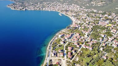 An aerial view of a coastal town with a clear blue sea, surrounded by mountains and residential areas.