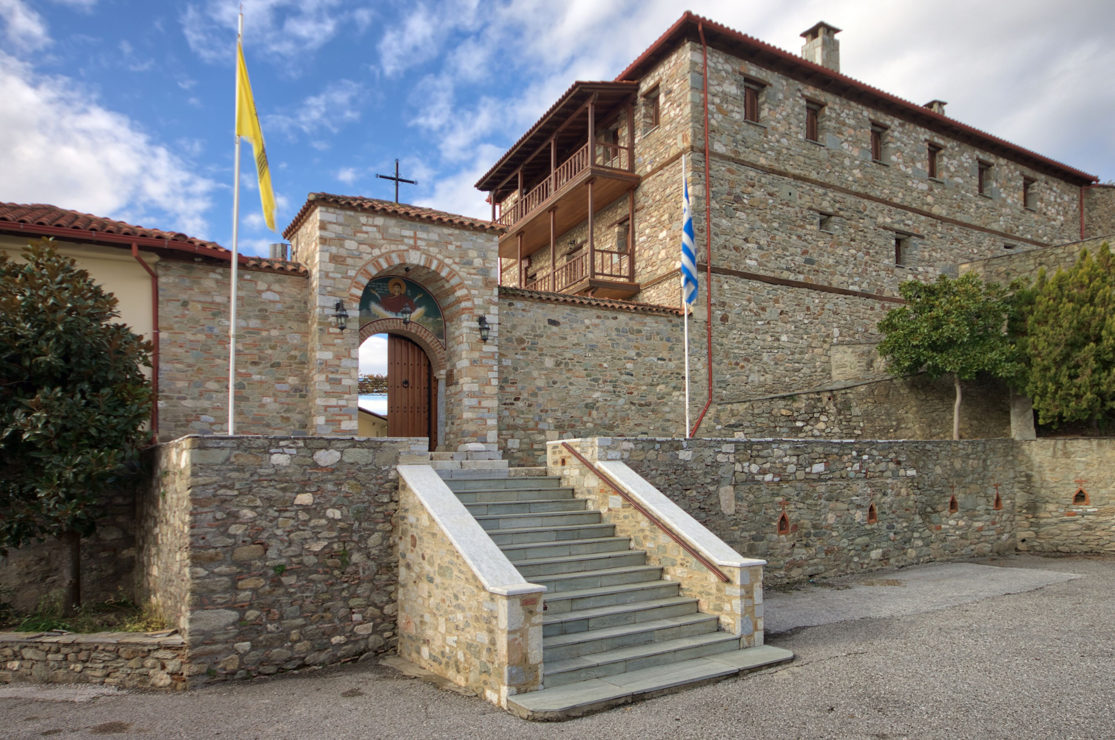 A stone building with a wooden staircase leading to a door, a flagpole, and a balcony.