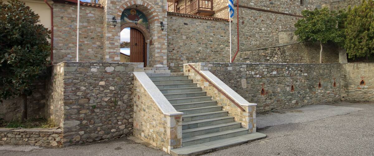 A stone building with a wooden staircase leading to a door, a flagpole, and a balcony.