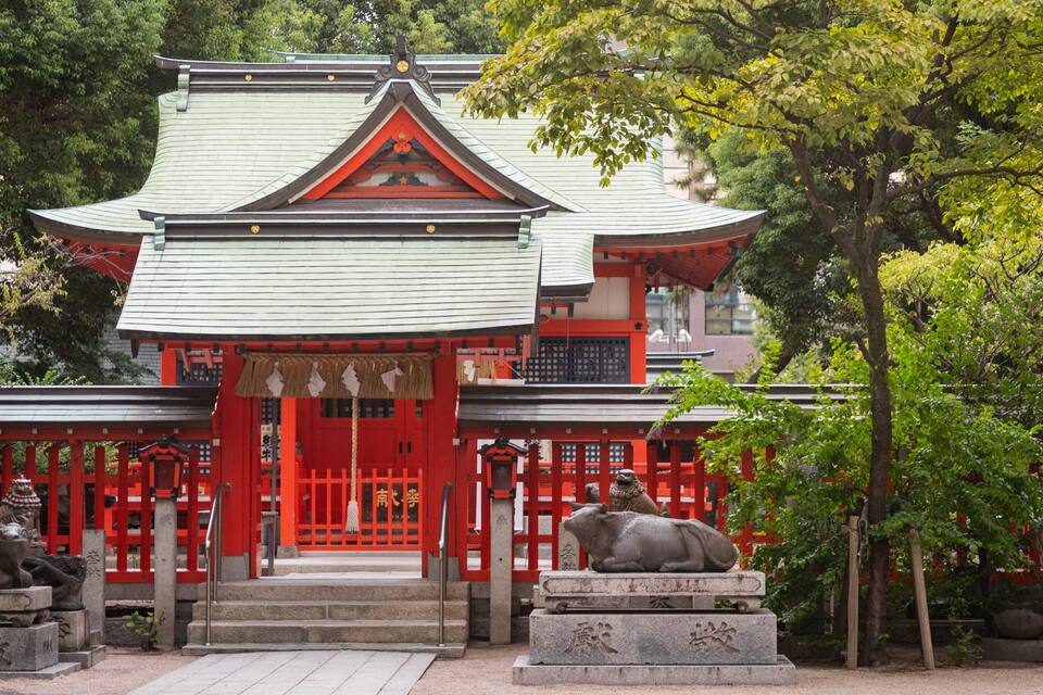 A traditional Japanese temple with a red gate, stone lion statues, and a green roof.