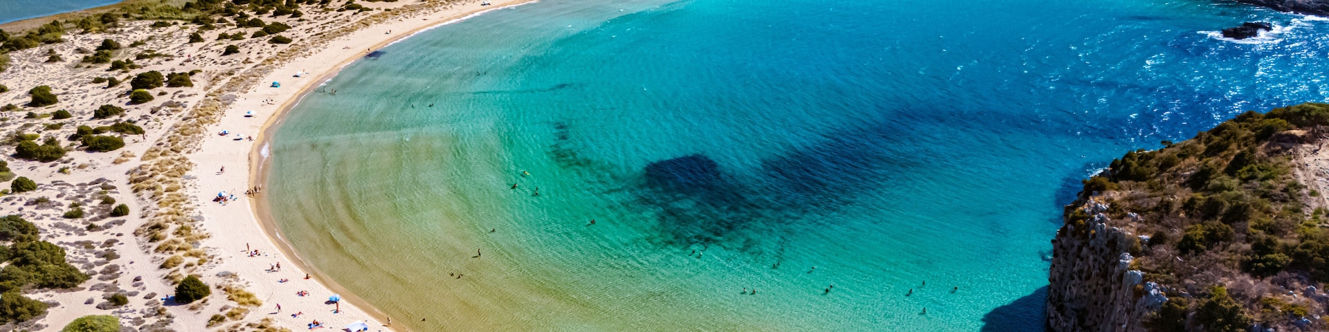 Eine KĂŒstenlandschaft mit einer geschwungenen Bucht, klarem tĂŒrkisblauem Wasser, SandstrĂ€nden und felsigen Klippen.