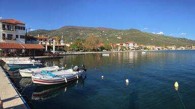 A harbor with boats docked, a waterfront promenade, and a backdrop of hills and buildings.