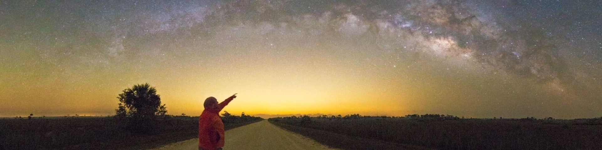 Una persona parada en un camino rural bajo un cielo estrellado, con la Vía Láctea visible.