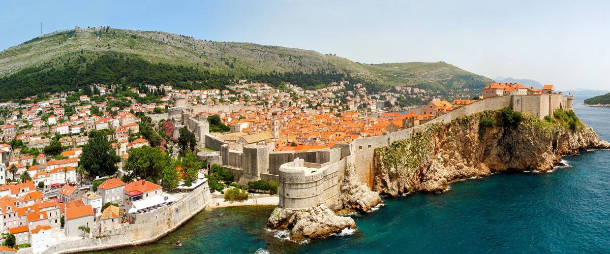A coastal city with historic fortifications, terraced houses, and a mountainous backdrop.