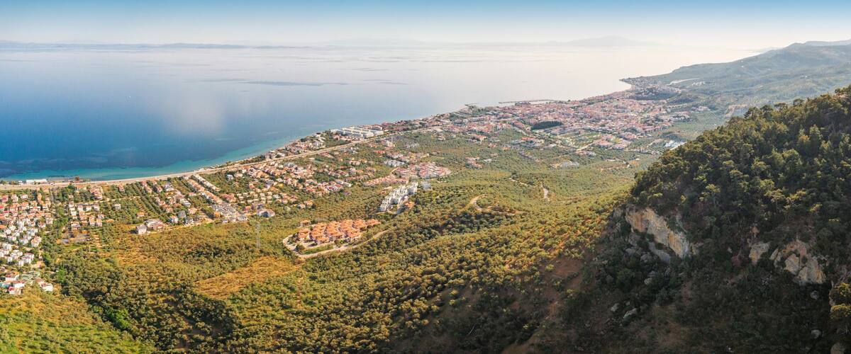 A coastal town with dense housing, a clear coastline, and a forested mountain.