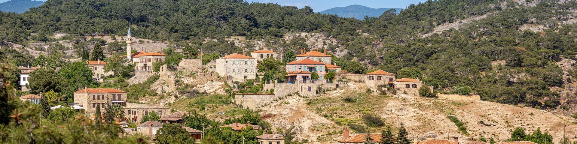 Picturesque view of Adatepe village, showcasing traditional stone houses nestled amidst lush greenery and rolling hills, creating a serene scene