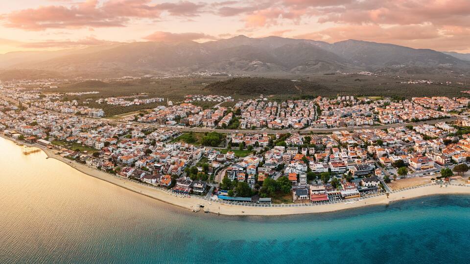 A coastal town with a beach, houses, and mountains in the background.