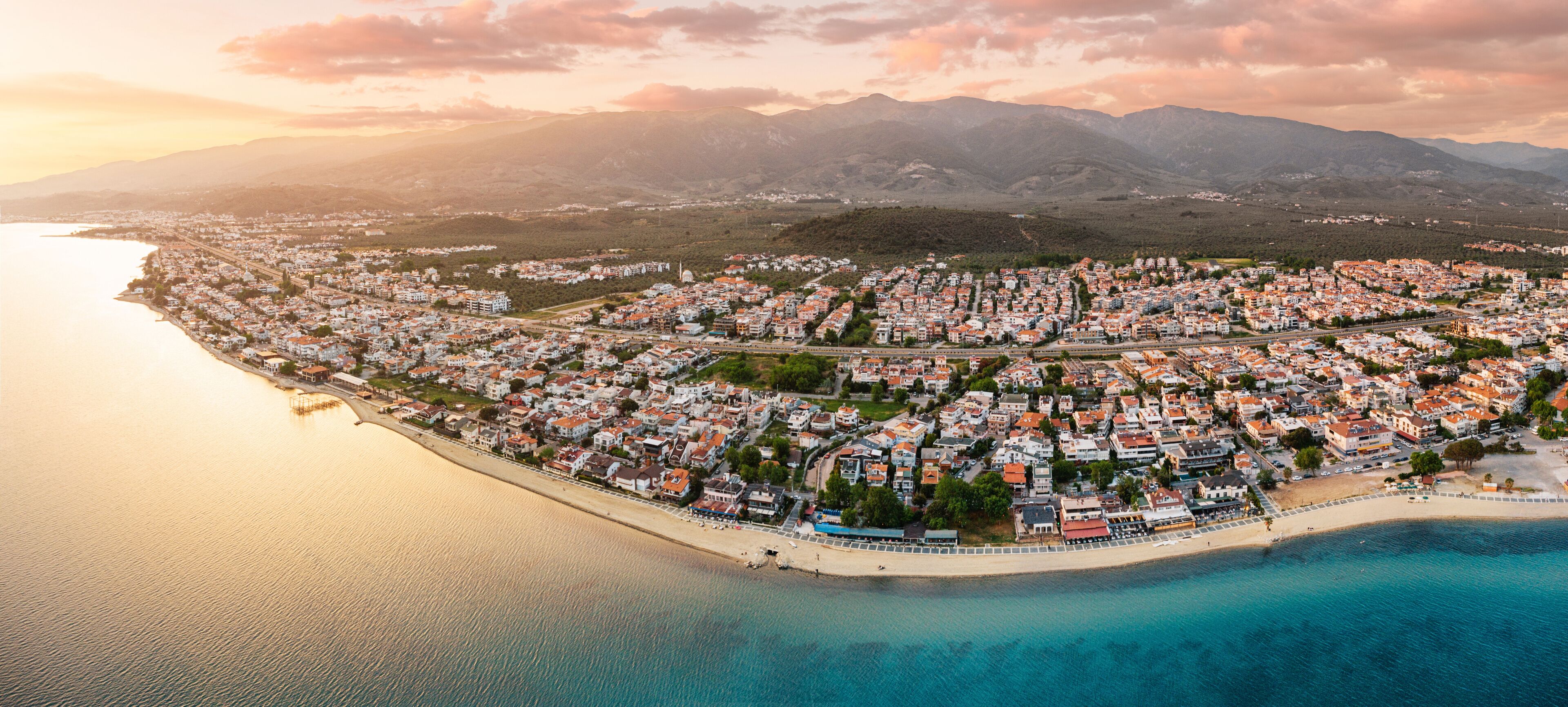 A coastal town with a beach, houses, and mountains in the background.