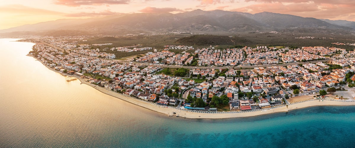 A coastal town with a beach, houses, and mountains in the background.