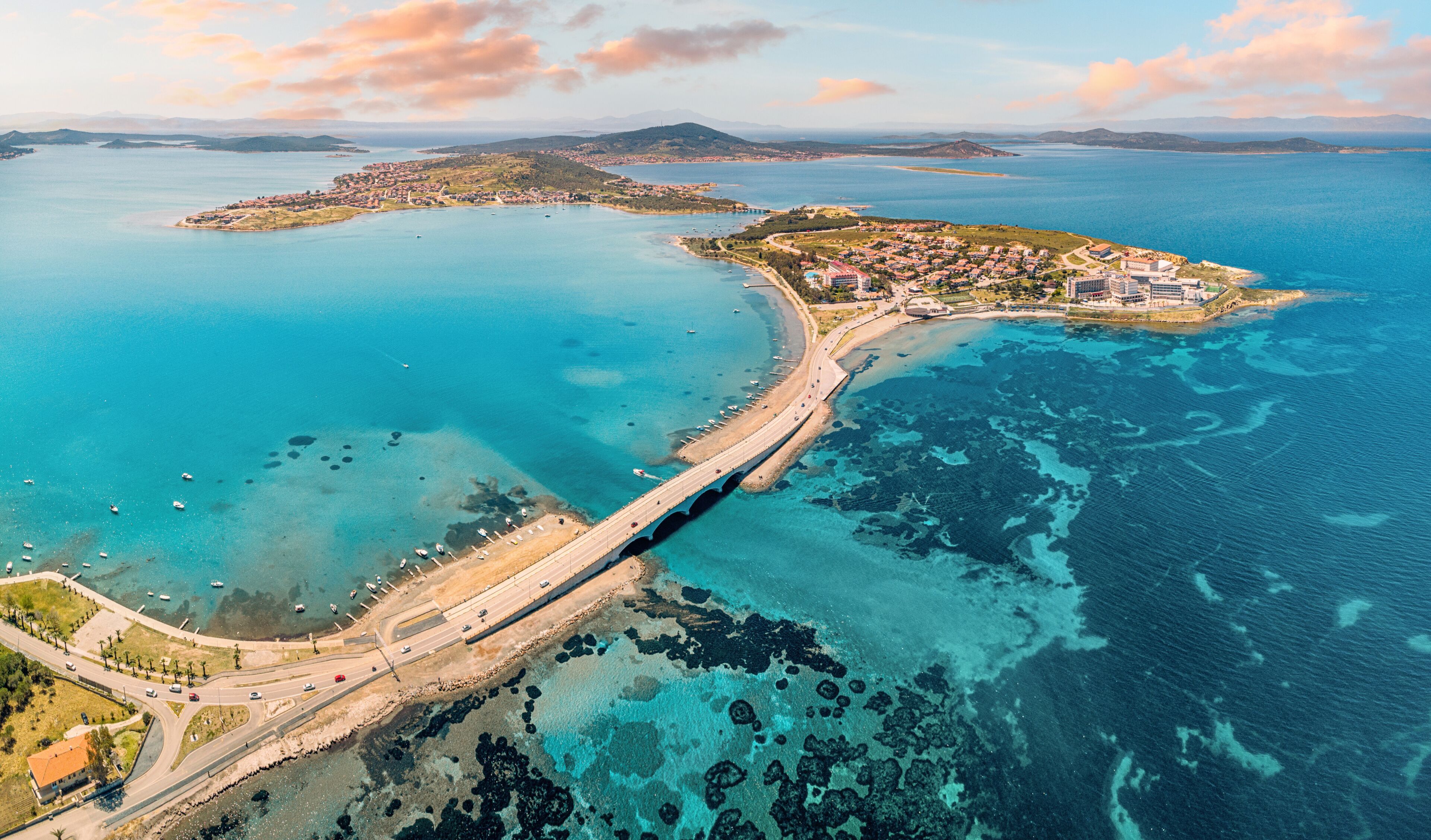 Panoramic aerial view of Cunda Island and Ayvalik, Turkiye, connected by a bridge, showcasing the vibrant turquoise Aegean Sea and coastal town