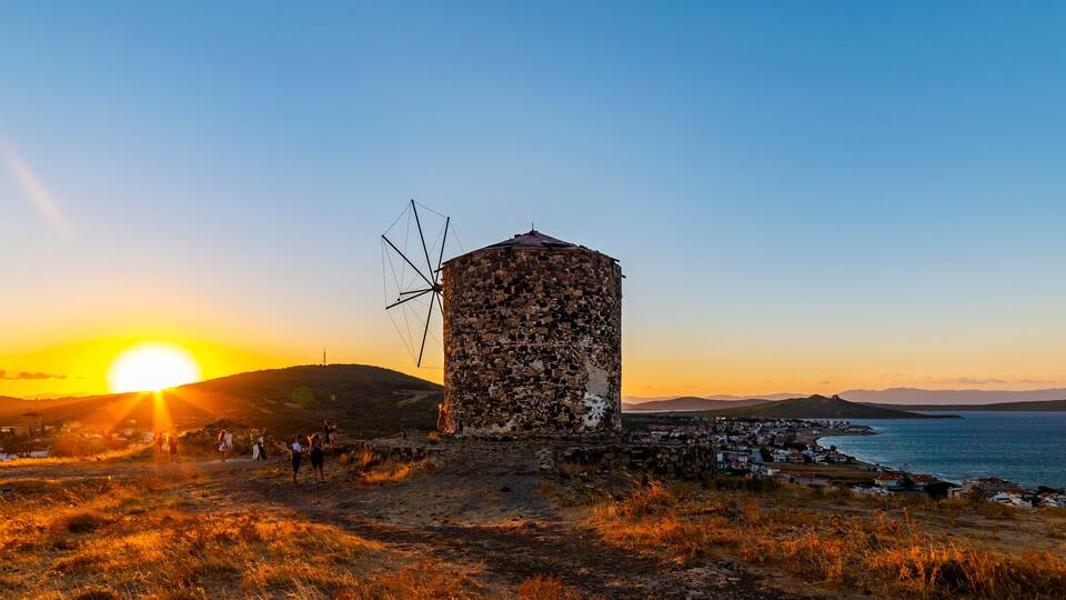 Un moulin à vent, une ville côtière et un coucher de soleil sur la mer.