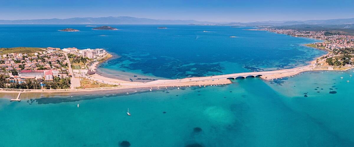 Scenic aerial view of the bridge connecting Cunda Island to mainland Ayvalik, Turkey, with boats and clear turquoise sea