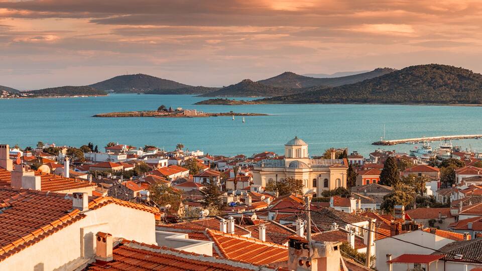Un pueblo costero con tejados de terracota, una iglesia destacada y una vista despejada del mar y colinas lejanas.