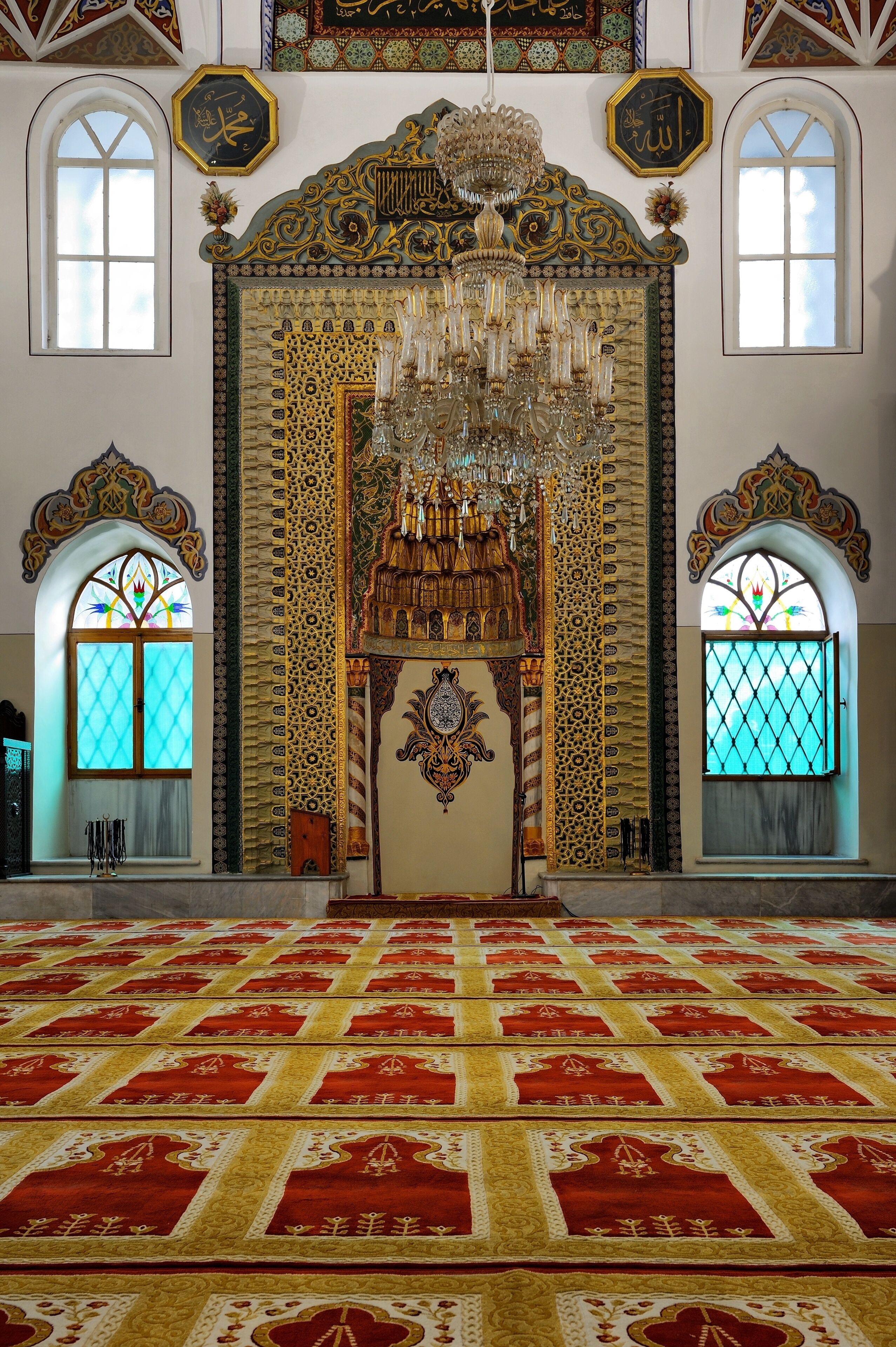 Un interior ornamentado con una gran lámpara de araña, decoraciones intrincadas en las paredes y un piso cubierto de alfombra roja.